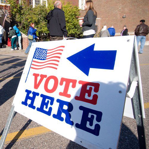 people walking around a sign that says vote here