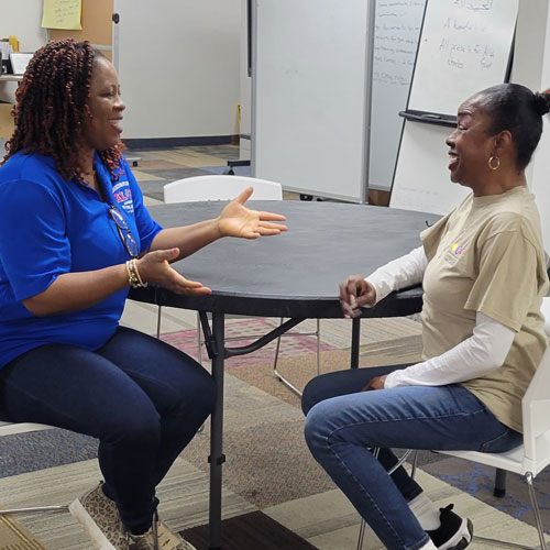 Two women smiling and having a conversation at a small, round table.