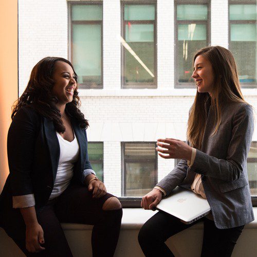 Two women sitting on a window sill and talking