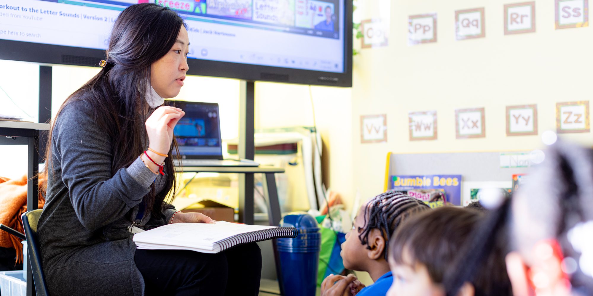 teacher sitting with book in front of students