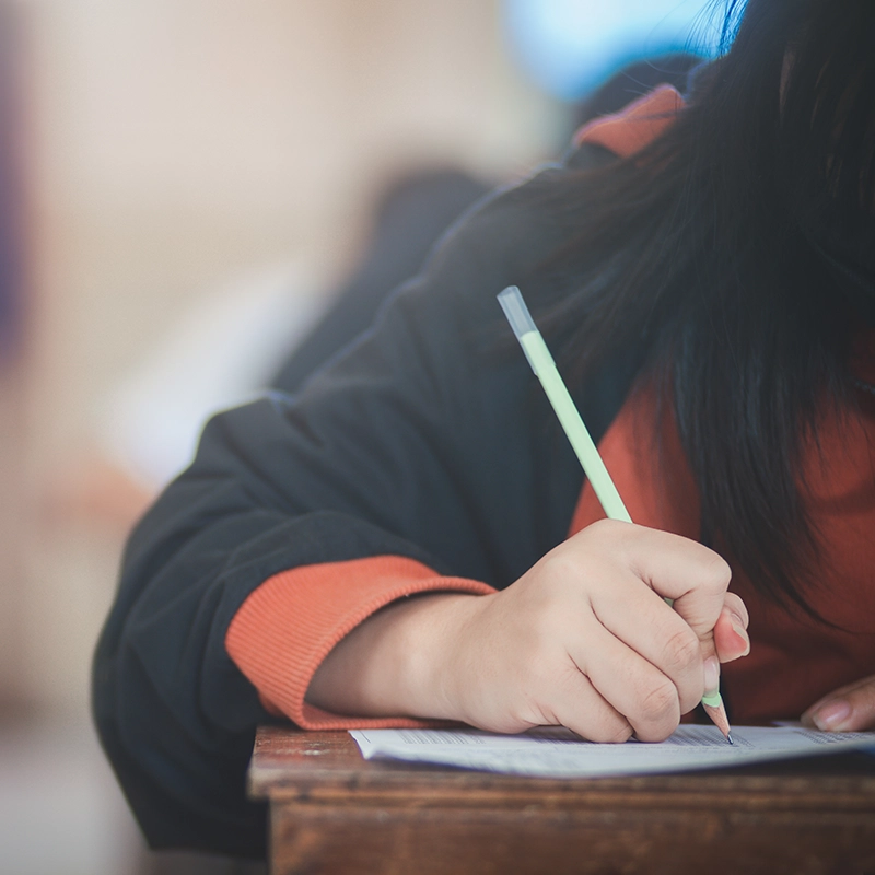 Close up of a student's hand at desk writing notes.